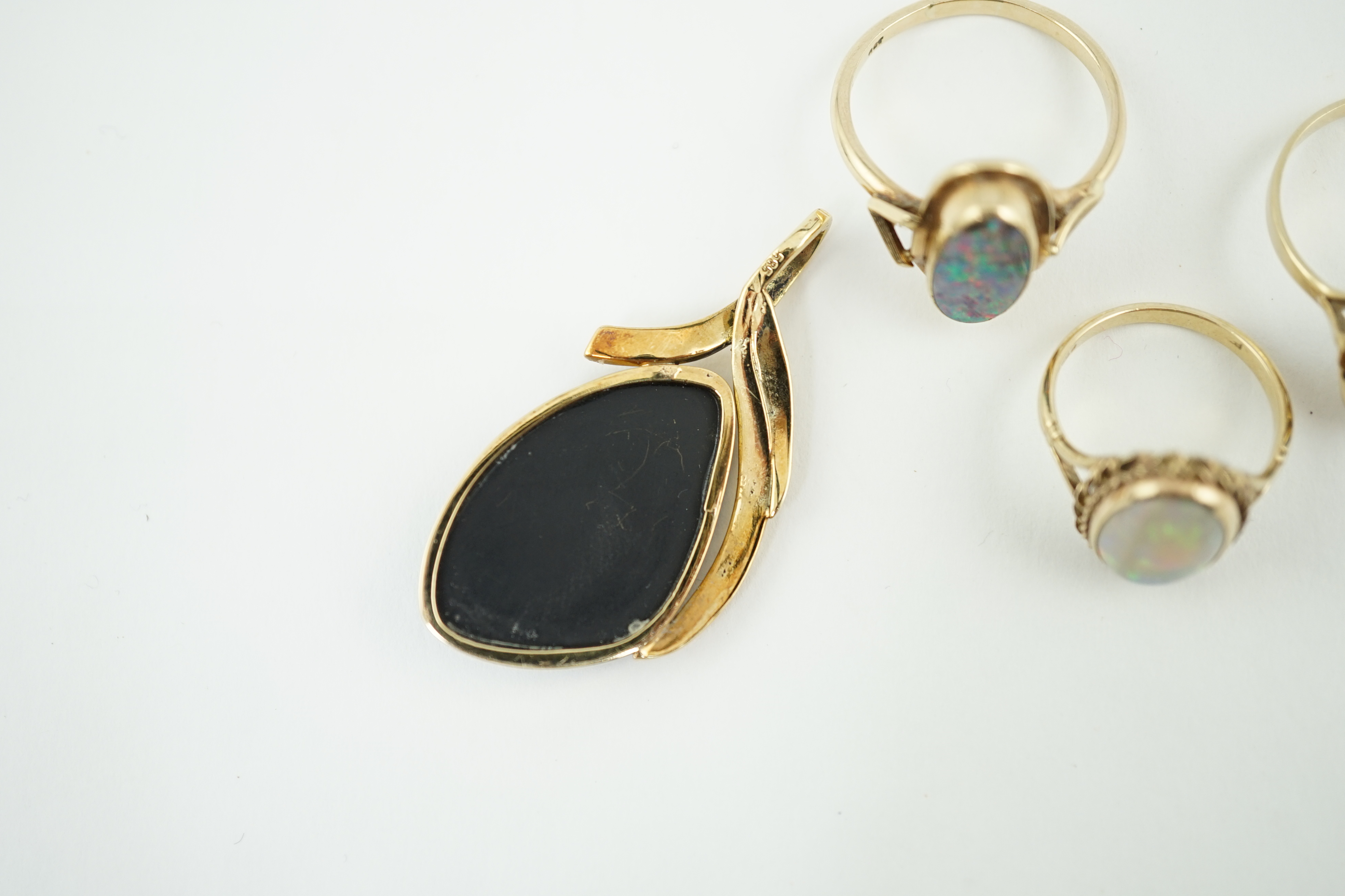 A modern 14k gold and black opal set pendant, 44mm, together with three assorted 9ct gold and single stone cabochon opal set rings